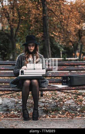 Weibliche Schriftsteller mit Schreibmaschine, während auf der Bank im Park sitzen im Herbst Stockfoto