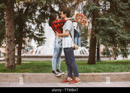 Volle Länge des jungen Paares romancing auf Fußweg gegen Bäume in der Stadt Stockfoto