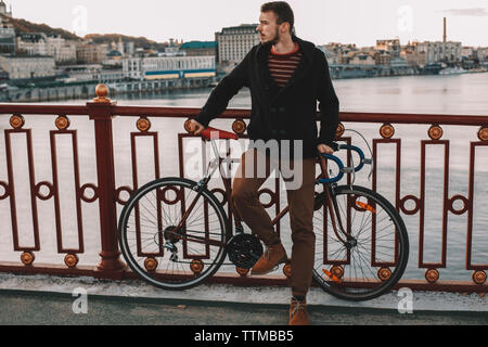 Radfahrer weg schauen, während man mit dem Fahrrad auf Brücke über den Fluss in die Stadt bei Sonnenuntergang Stockfoto