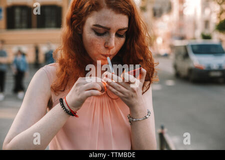 Junge Frau mit Sommersprossen Beleuchtung Zigarette, während in der Straße stehend Stockfoto