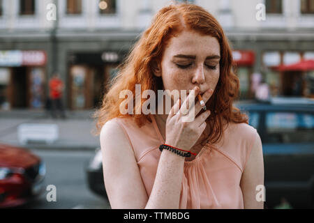 Junge Frau mit Sommersprossen rauchen Zigarette, während in der Straße stehend Stockfoto