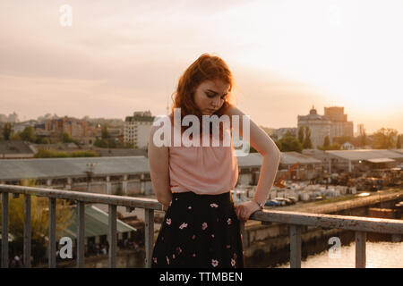 Junges Mädchen mit roten Haaren steht auf Brücke bei Sonnenuntergang Stockfoto