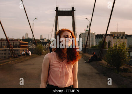 Glückliches Mädchen mit roten Haaren steht auf der Brücke in der Stadt Stockfoto