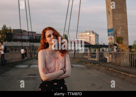 Porträt der jungen Frau mit roten Haaren steht auf der Brücke in der Stadt
