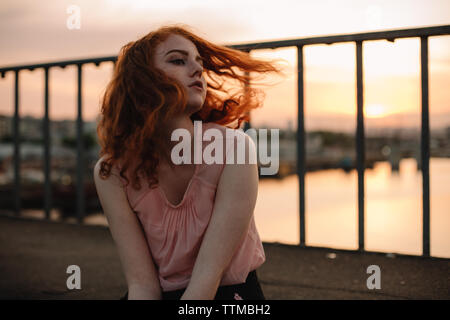 Red head Jugendmädchen werfen Haar, während auf der Brücke bei Sonnenuntergang sitzen Stockfoto