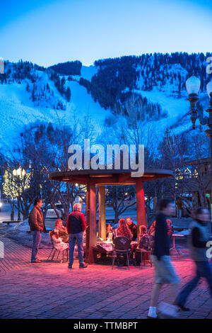 USA, Colorado, Aspen, Menschen warm up durch das Feuer in den Marktplatz in der Innenstadt von Aspen in der Dämmerung Stockfoto