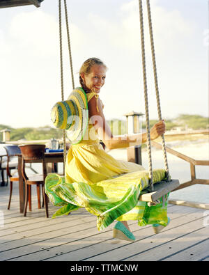 Aruba, Surfside Marina, eine junge Frau sitzt auf einem Schwingen an Pinchos Bar & Grill lächelnd Stockfoto