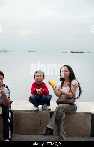 Philippinen, Manila, Familie genießt einige Mais am Rojas Blvd Bay zu Fuß Stockfoto