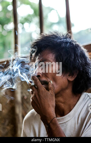 Philippinen, Palawan, Barangay region, Batak Mann namens Arturo Sapitanan in Kalakwasan Dorf raucht Stockfoto