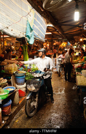 VIETNAM, Hanoi, Chau Long Markt, ein Mann reitet ihn durch den Markt Moped- und hält einige Kartoffeln kaufen Stockfoto
