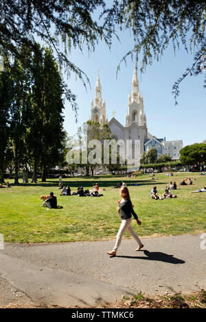 USA, Kalifornien, San Francisco, eine Frau geht durch die Leute sitzen auf dem Rasen und geniessen Sie den Nachmittag und das Washington Square Park Stockfoto