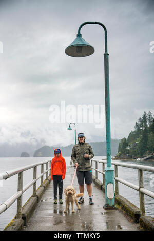 Kanada, Vancouver, British Columbia, Vater und Sohn stehen mit ihrem Hund auf dem Pier in Deep Cove, North Vancouver Stockfoto