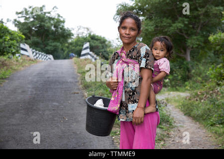 Indonesien, Flores, eine Frau und ihr Baby stehen auf der Seite der Straße im Dorf Dintor Stockfoto