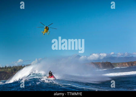 USA, Hawaii, Maui, Backen, einem schwebenden Hubschrauber über den großen Wellen und Surfer an Peahi auf dem Northshore Stockfoto