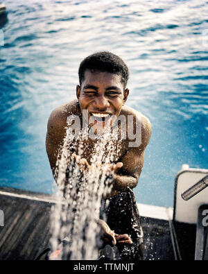 Fidschi, nördlichen Lau Inseln, ein junger Mann nimmt einen Spülen auf der Rückseite Deck eines Fischerboot Stockfoto