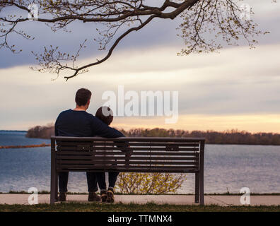 Vater und Sohn zu betrachten, während das Sitzen auf einer Parkbank am See Stockfoto