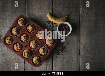 Hohe Betrachtungswinkel von gebackenen Muffins in Backblech mit Schokolade und Banane auf hölzernen Tisch zu Hause Stockfoto