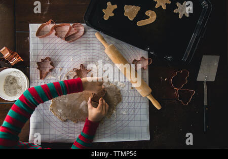 Abgeschnittene Hände eines Jungen mit einem Teigschneider, während er während der weihnachtszeit zu Hause Kekse auf dem Tisch macht Stockfoto