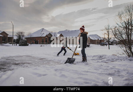 Brüder schaufeln Schnee auf der Straße gegen Häuser Stockfoto