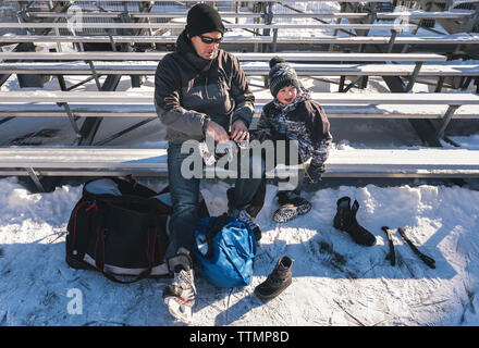 Hohe Betrachtungswinkel und der Vater, der Sohn Schnürsenkel binden, während sitzt auf der Bank im Winter Stockfoto