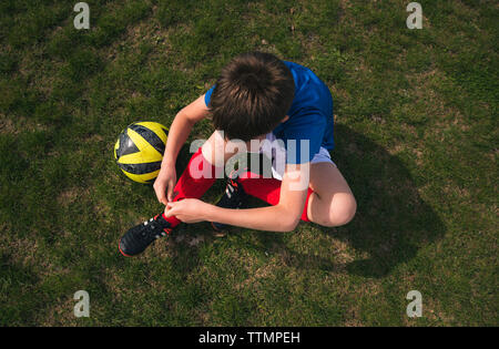 Hohe Betrachtungswinkel von boy Schnürsenkel binden beim Sitzen auf Fußball-Feld Stockfoto