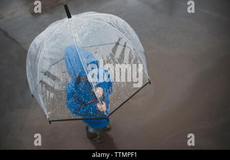 Hohe Betrachtungswinkel der Boy mit Schirm stehen auf der Straße während der Regenzeit Stockfoto