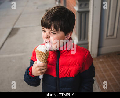 Junge weg schauen, während Lecken Eis auf Wanderweg in Stadt Stockfoto