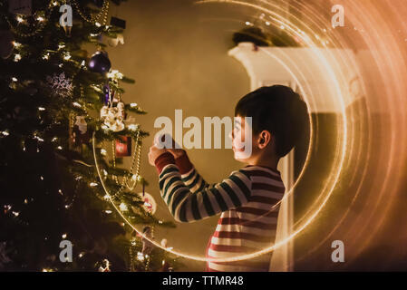 Nahaufnahme eines Jungen schmücken einen Weihnachtsbaum in der Nacht. Stockfoto