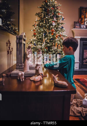 Junge Junge an der Krippe mit Weihnachtsbaum hinter ihm. Stockfoto