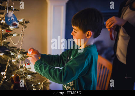 Junge hängt Dekoration auf den Weihnachtsbaum. Stockfoto