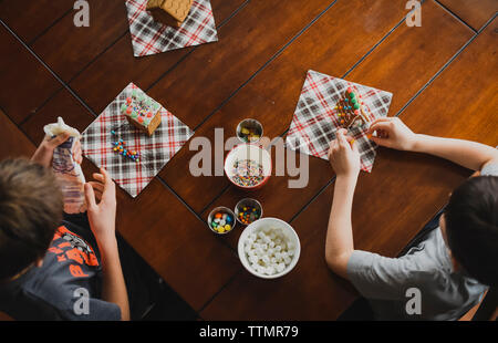 Overhead shot von zwei Jungen dekorieren Lebkuchenhäuser auf einen Tisch. Stockfoto