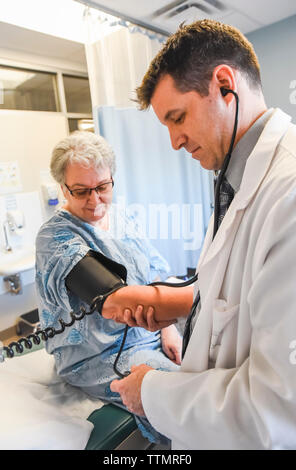 Arzt unter Blutdruck von älteren Patienten mit Kleid in der Klinik. Stockfoto