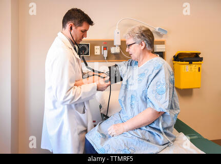 Arzt unter Blutdruck von älteren Patienten mit Kleid in der Klinik. Stockfoto