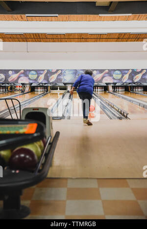 Vertikale Bild der älteren Frau werfen Bowling Kugel unten Bowlingbahn. Stockfoto