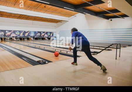 Ältere Frau werfen Bowling Kugel unten eine Bowlingbahn. Stockfoto