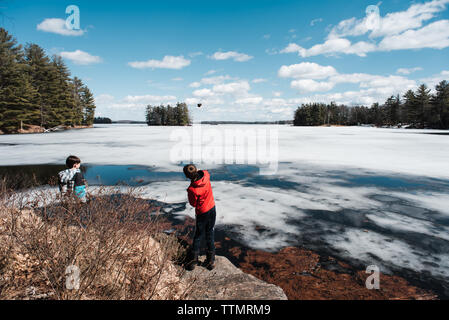 Zwei Jungen werfen Steine auf das Eis auf einem See an einem Frühlingstag. Stockfoto