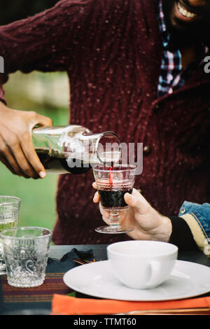 Mittelteil des Menschen gießen Wein für Freund in Glas, beim Sitzen am Tisch Stockfoto