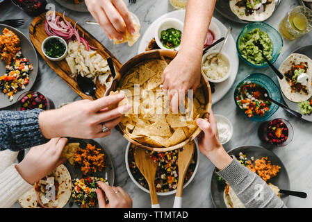 7/8 Hand von Freunden, Nacho Chips beim Essen am Tisch Stockfoto
