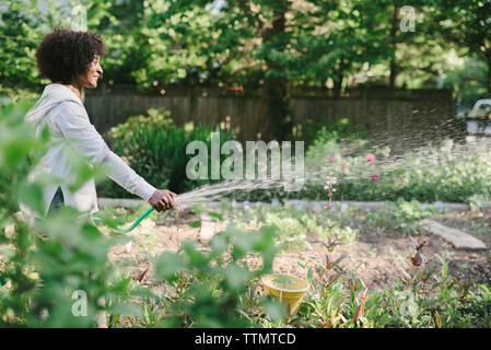 Seitenansicht der reifen Frau Bewässerung von Pflanzen im Garten Stockfoto