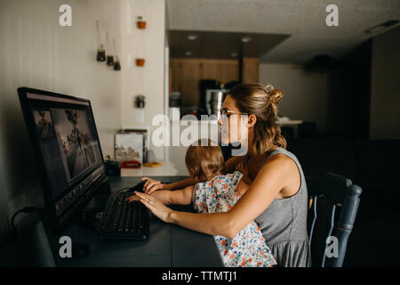 Multitasking Working Mother Holding Baby und geben Sie auf dem Computer Stockfoto