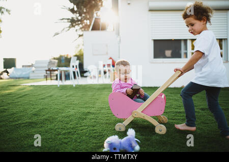 Große Schwester tragen ihre kleine Schwester in einem doll Stroller im Hof Stockfoto