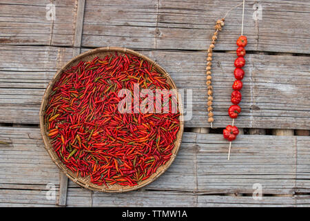 Hohe Betrachtungswinkel von red chili peppers in Weidenkorb von Tomaten auf Holzboden Stockfoto