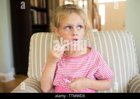 Mädchen Anwendung Lip Gloss beim Sitzen auf einem Sessel zu Hause Stockfoto