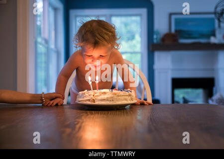 Bei Kerzenschein Toddler Boy Ausblasen Kerzen auf der Geburtstagstorte Stockfoto