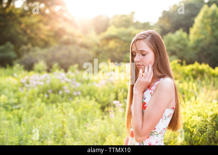 Schöne Mädchen im Teenageralter mit geschlossenen Augen steht im Feld im Sonnenlicht Stockfoto