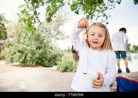 Cute girl Holding Stick während Bruder steht im Hintergrund am Seeufer Stockfoto