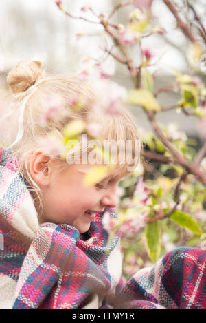 Nahaufnahme der lächelnde Mädchen in Decke sitzen durch Pflanzen im Hof gewickelt Stockfoto