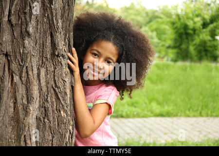 Afroamerikanische Mädchen versteckt sich hinter Baum im Park Stockfoto