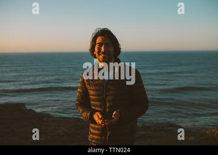 Portrait von glücklichen Mann, smart phone beim Stehen vor der See bei Sonnenuntergang Stockfoto