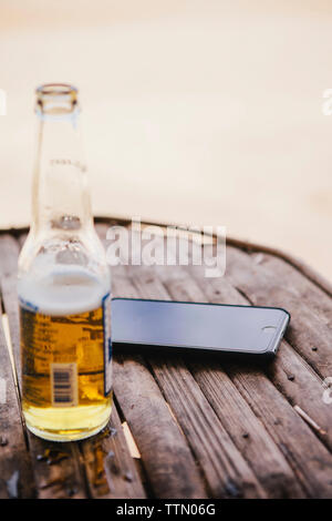 Hohe Betrachtungswinkel von Handy und Bier Flasche auf dem Tisch am Strand Stockfoto